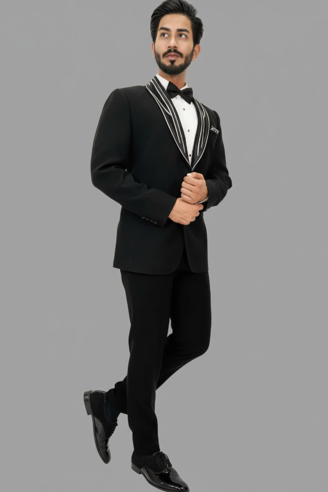 Man wearing a black tuxedo with white trim on a gray background