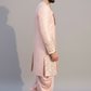 Man wearing a traditional pink sherwani with intricate embroidery on a plain background