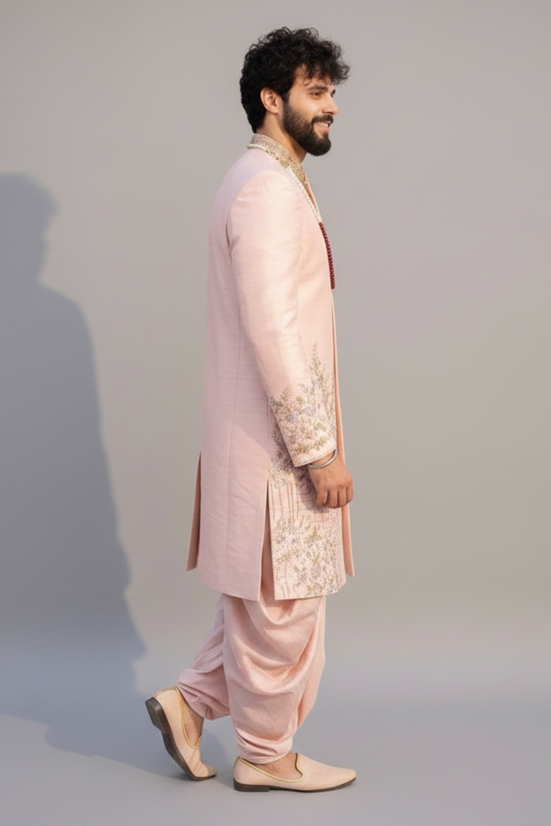 Man wearing a traditional pink sherwani with intricate embroidery on a plain background