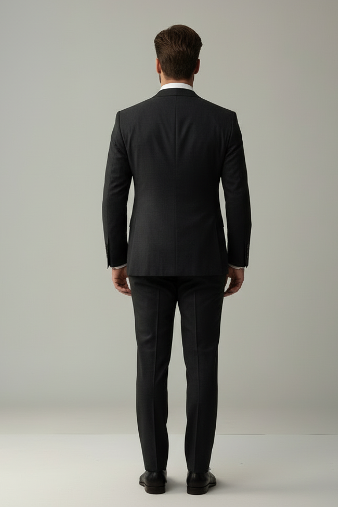 Man wearing a black suit standing against a plain background