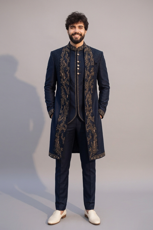 Man wearing a dark blue embroidered sherwani with white shoes on a gray background