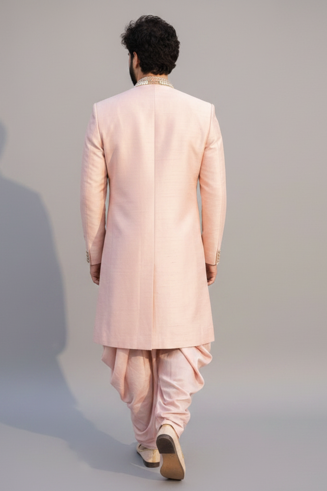 Man wearing a light pink traditional outfit on a plain background