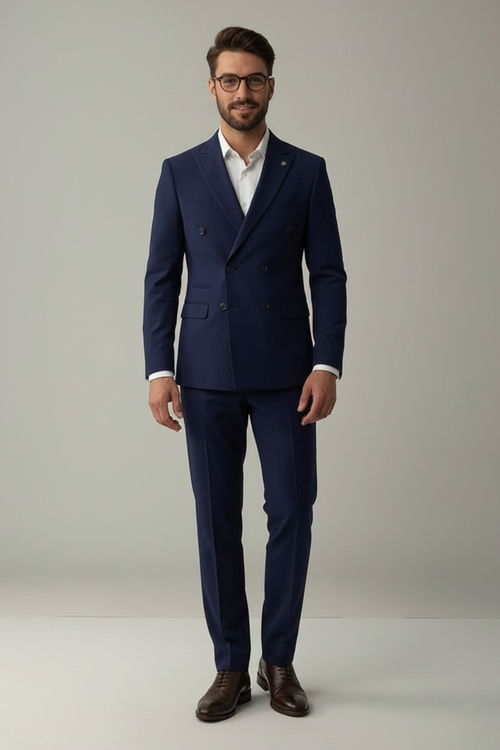 Man wearing a navy suit with a white shirt and brown shoes on a plain background