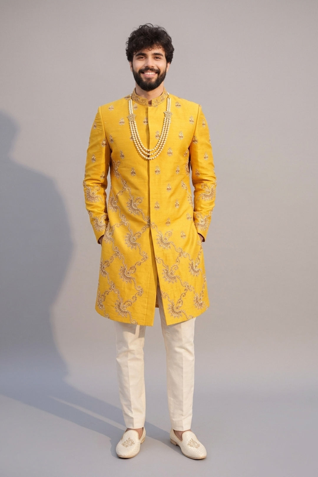 Man wearing a yellow embroidered sherwani with white pants on a gray background