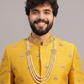 Man wearing a yellow embroidered traditional outfit with a gray background