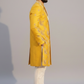 Man wearing a yellow embroidered sherwani with white pants on a gray background