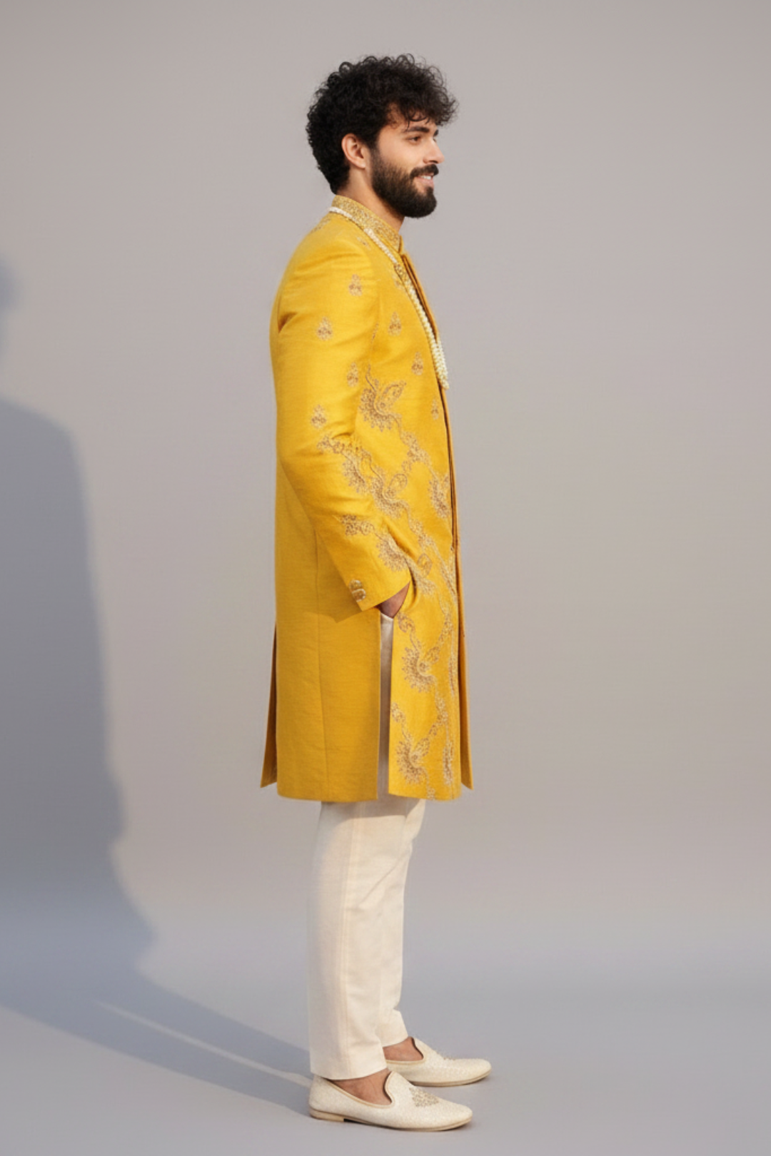 Man wearing a yellow embroidered sherwani with white pants on a gray background