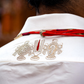 White shirt with intricate gold embroidery and a red ribbon on a blurred background