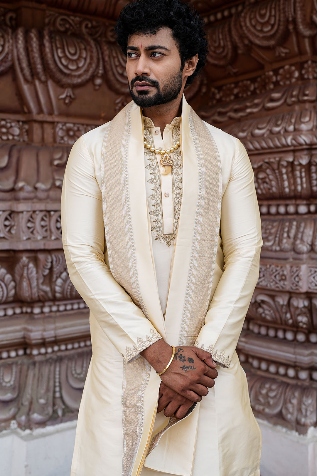 Man wearing a cream sherwani with intricate patterns in the background