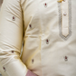 Close-up of a cream-colored traditional outfit with intricate patterns and a necklace.
