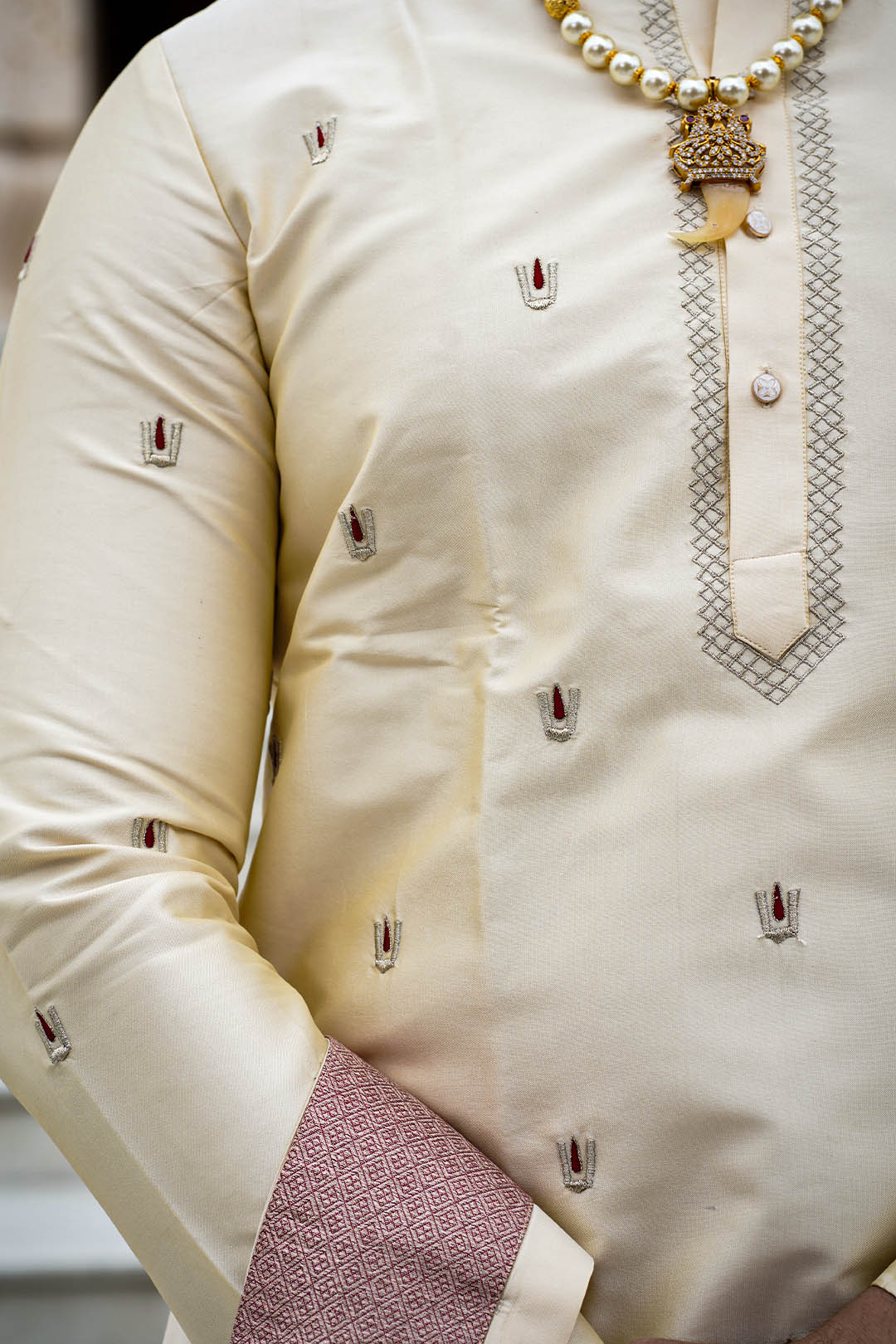 Close-up of a cream-colored traditional outfit with intricate patterns and a necklace.