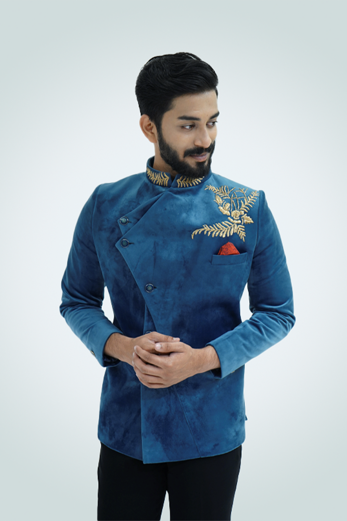 A man wearing a Teal Blue Velvet Jodhpuri with gold embellishments, paired with black trousers and tan shoes.