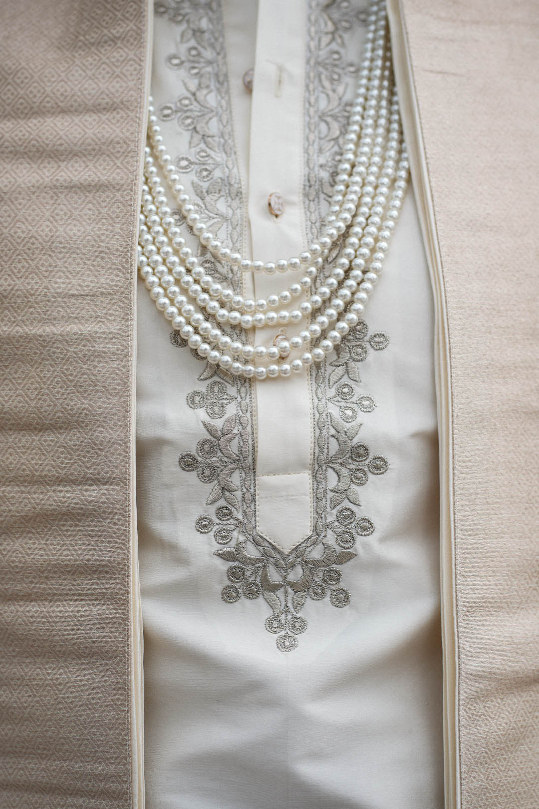 Close-up of a white embroidered garment with pearl necklaces on a beige background