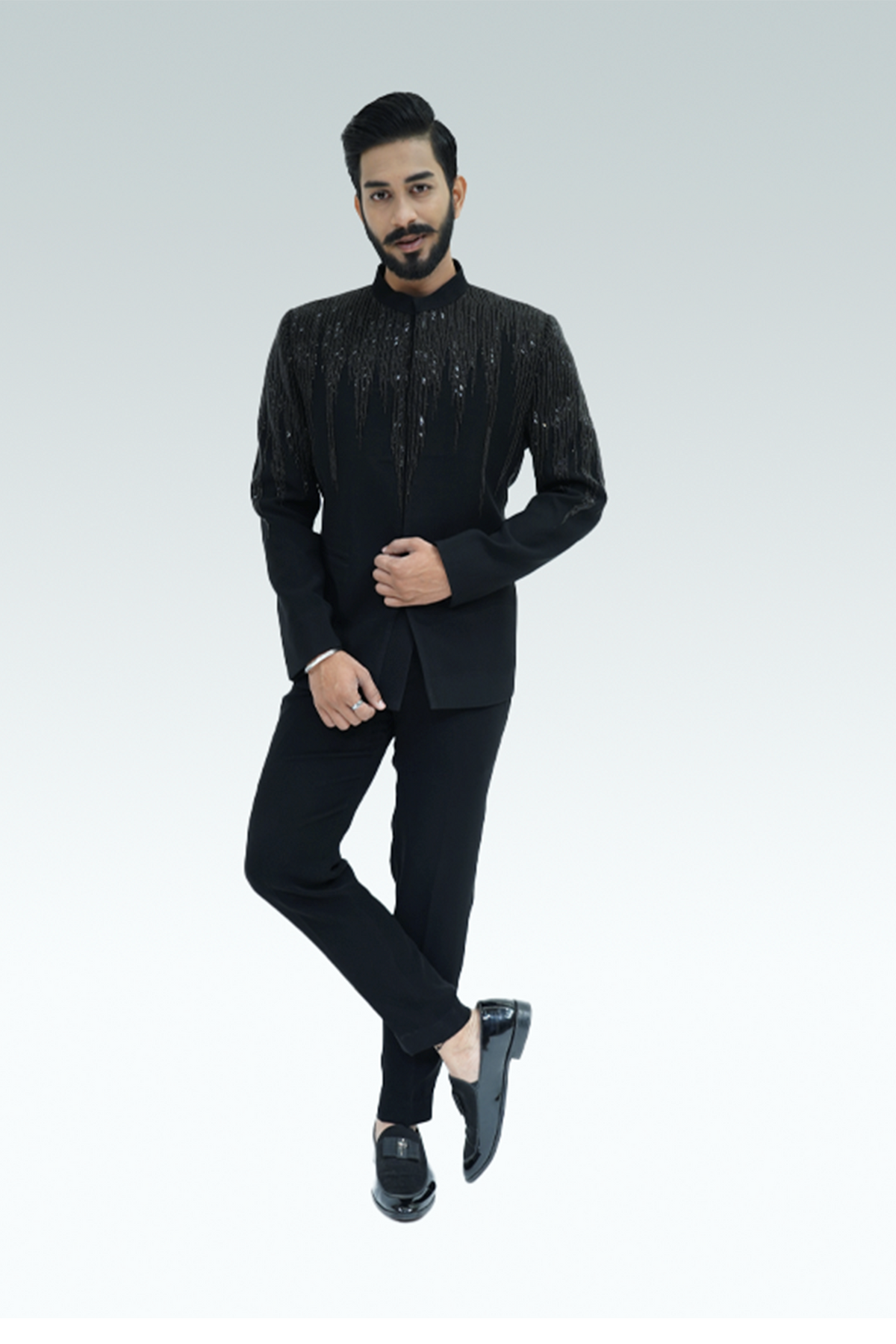 A man wearing a black shirt with wood crepe fabric and embellishments, paired with black trousers.
