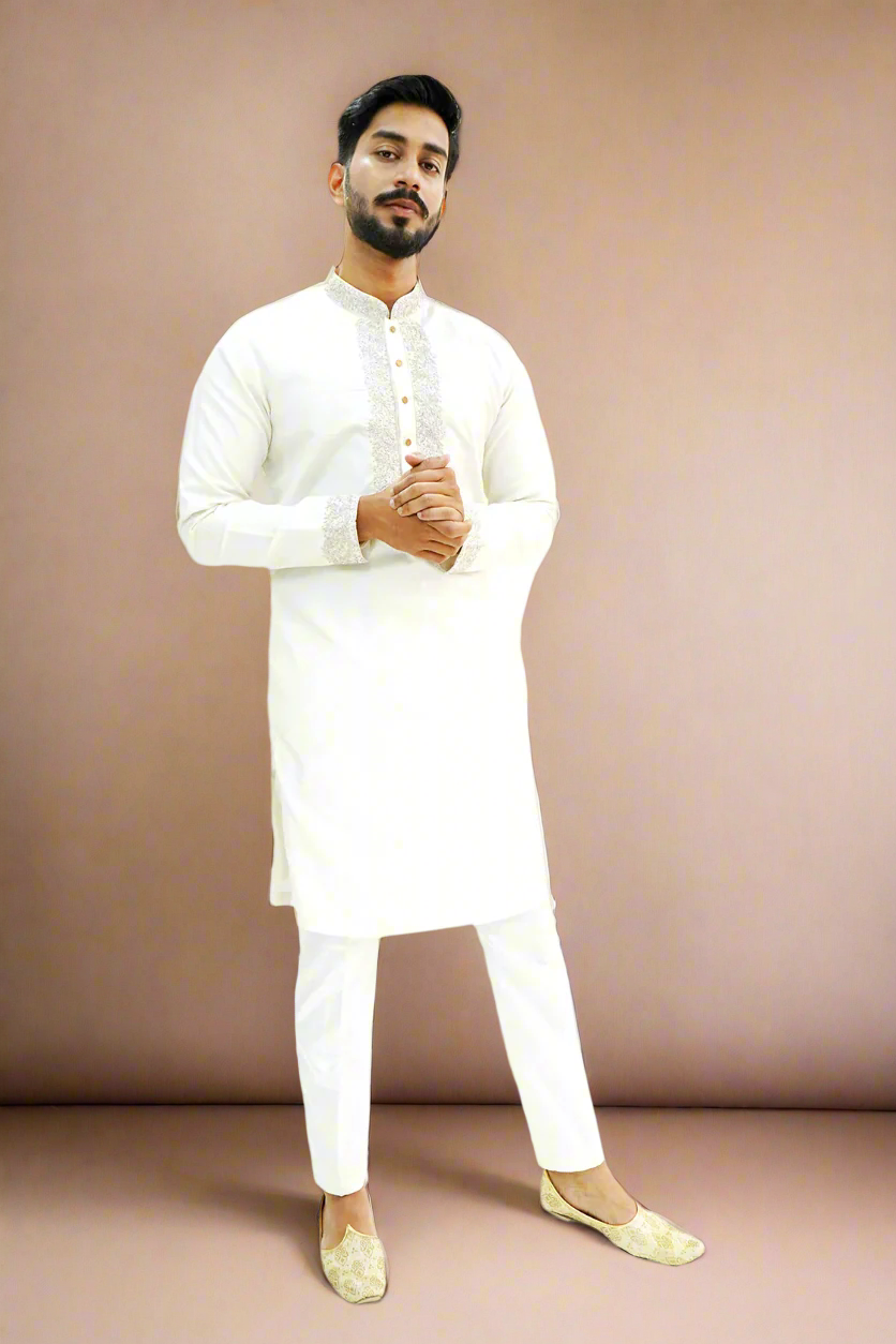 A man wearing an off-white semi-pattu kurta with zari embroidery, standing against a beige background.