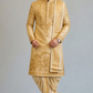 Man wearing a traditional gold sherwani with intricate patterns on a gray background