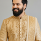 Man wearing a traditional embroidered beige sherwani against a gray background
