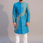 Man wearing a blue embroidered sherwani with white pants on a gray background