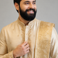 Man wearing a cream embroidered sherwani against a gray background