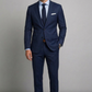 Man wearing a navy blue suit with a white shirt and brown shoes on a gray background