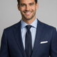 Man wearing a navy suit with a light blue shirt and dark tie on a gray background