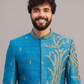 Man wearing a blue embroidered traditional outfit against a gray background
