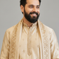 Man wearing a beige embroidered traditional outfit against a gray background