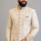 Man wearing a cream embroidered sherwani against a gray background