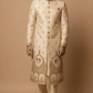 Man wearing a traditional embroidered sherwani against a beige background