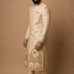 Man wearing a traditional embroidered sherwani against a beige background