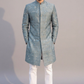Man wearing a light blue embroidered sherwani with white pants on a gray background