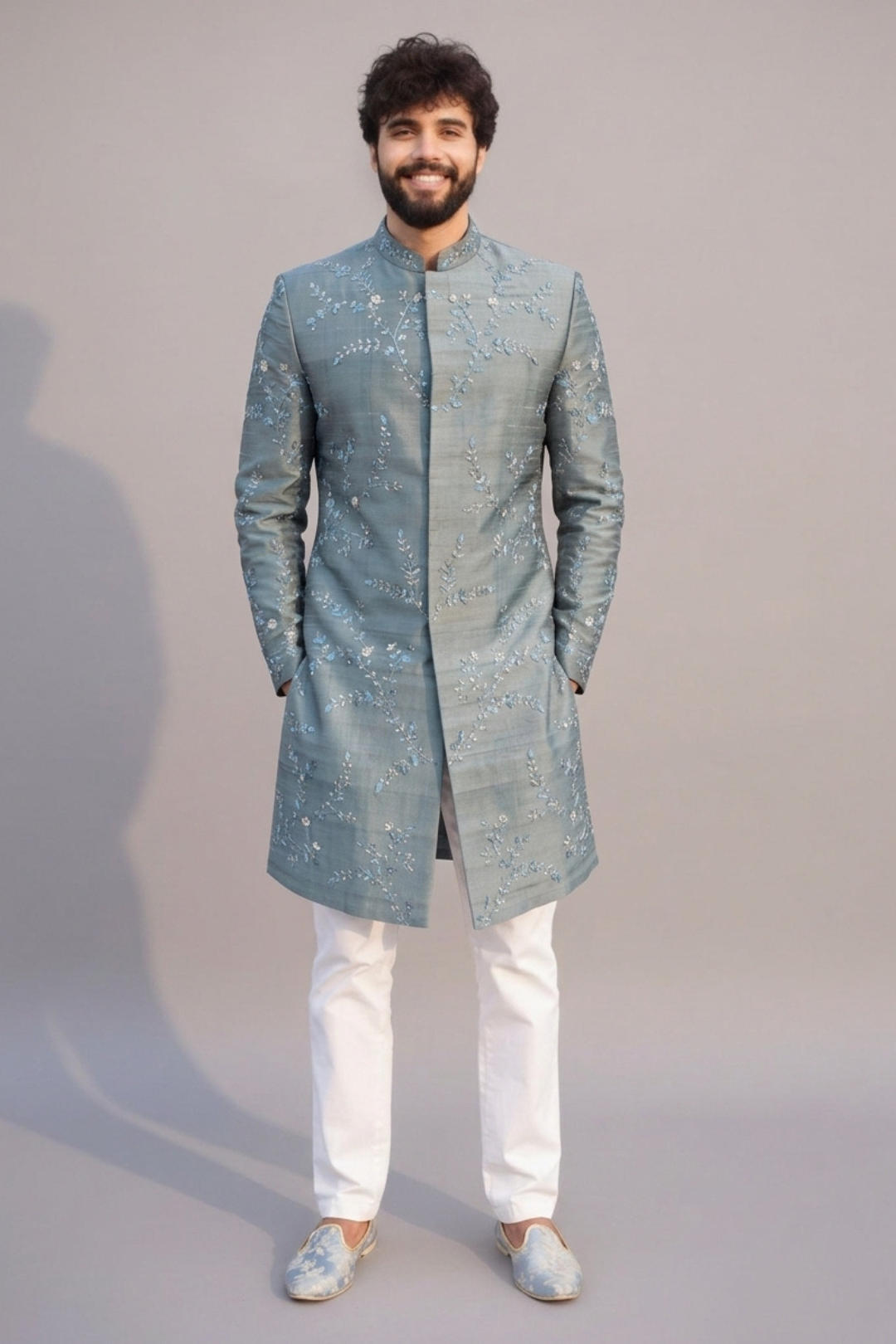 Man wearing a light blue embroidered sherwani with white pants on a gray background