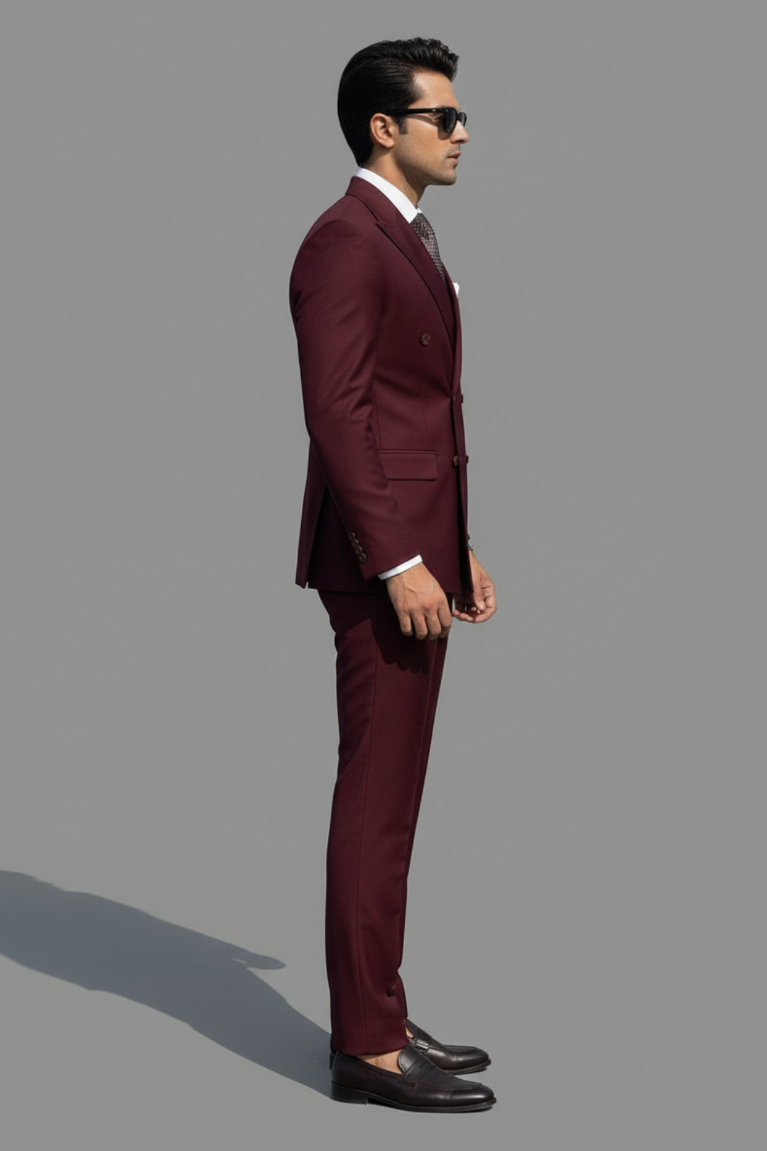 Man wearing a burgundy suit standing against a gray background