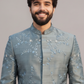 Man wearing a light blue embroidered traditional jacket against a plain background