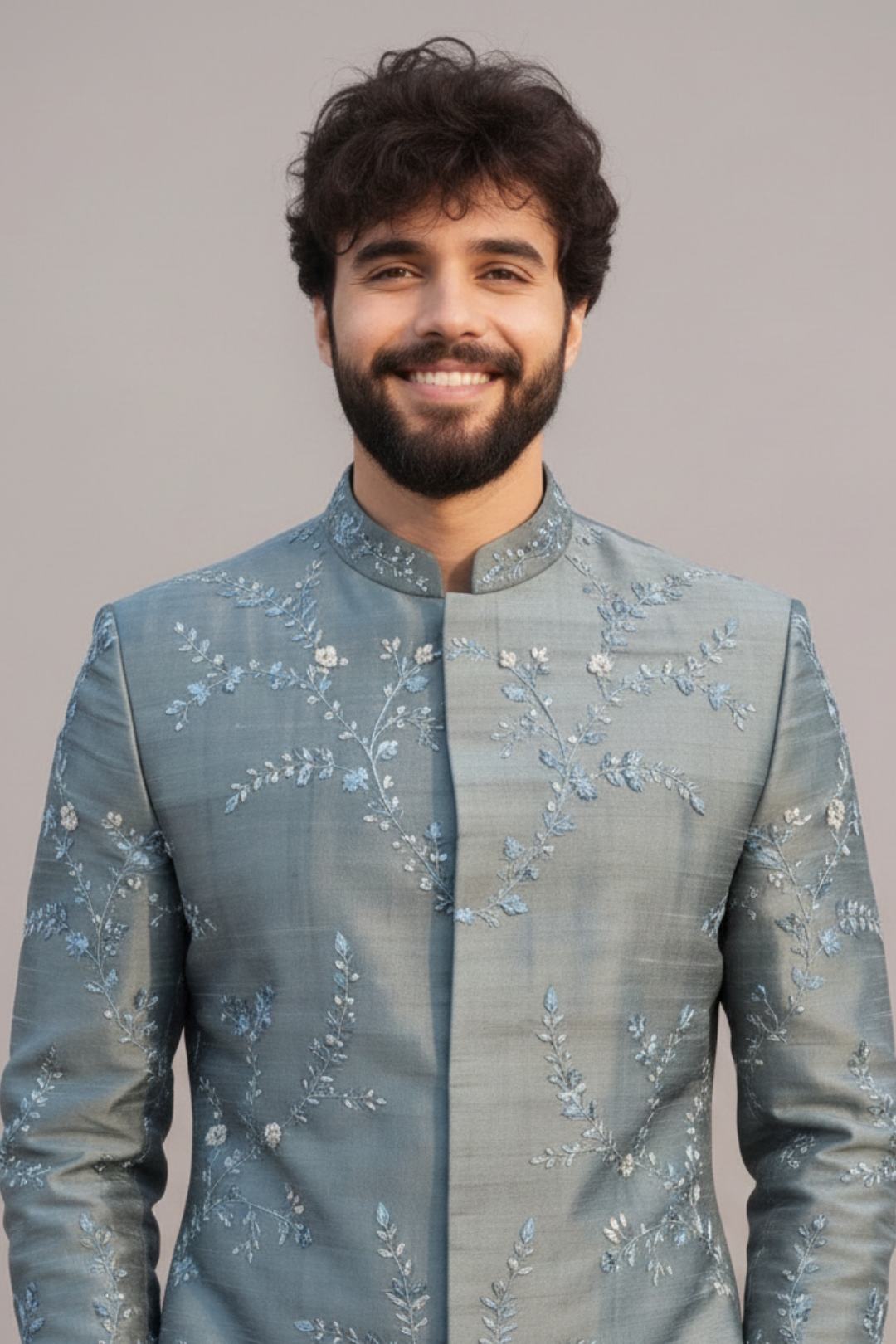 Man wearing a light blue embroidered traditional jacket against a plain background