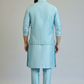Man wearing a light blue traditional outfit on a plain background