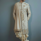 Man wearing a traditional embroidered sherwani against a plain background