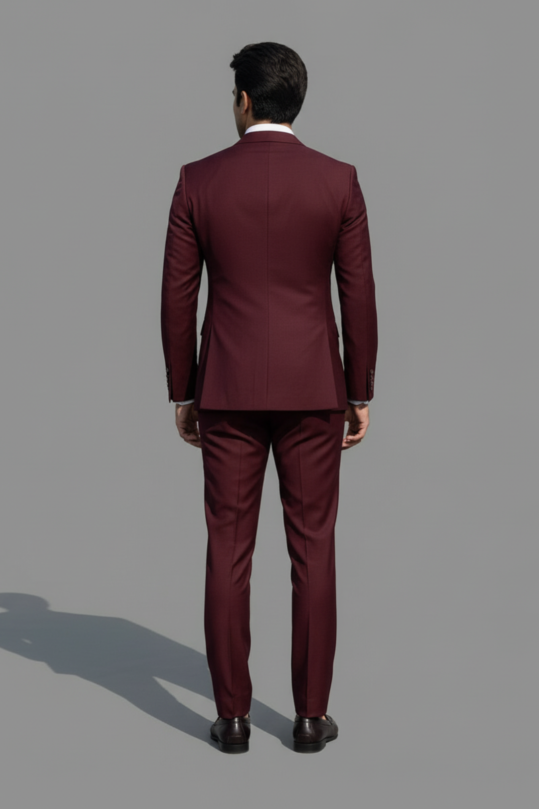 Man wearing a burgundy suit standing against a gray background