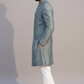 Man wearing a light blue sherwani with white pants on a plain background