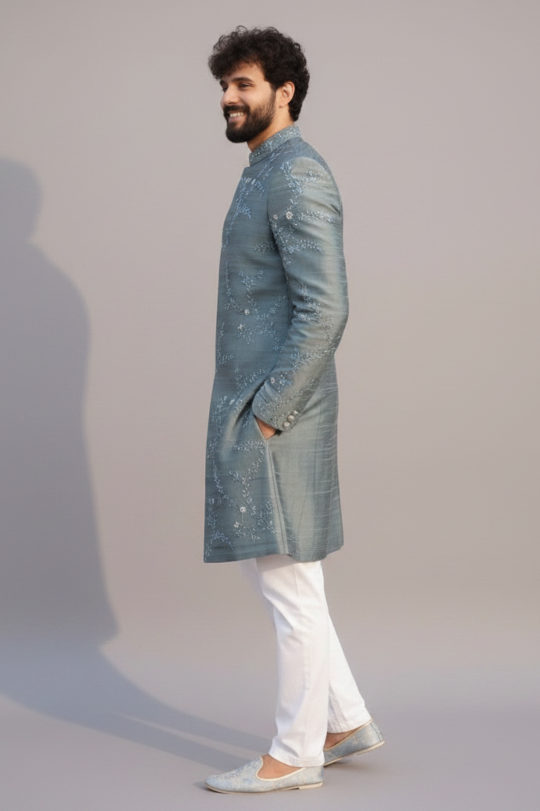 Man wearing a light blue sherwani with white pants on a plain background