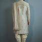 Man wearing a traditional beige sherwani with intricate embroidery on a gray background