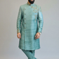 Man wearing a traditional green sherwani with intricate embroidery on a plain background
