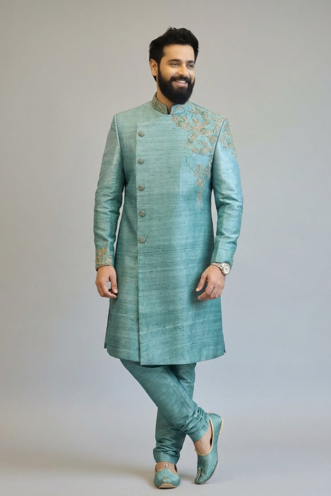 Man wearing a traditional green sherwani with intricate embroidery on a plain background