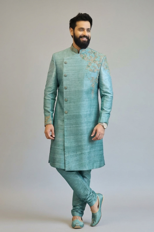 Man wearing a traditional green sherwani with intricate embroidery on a plain background