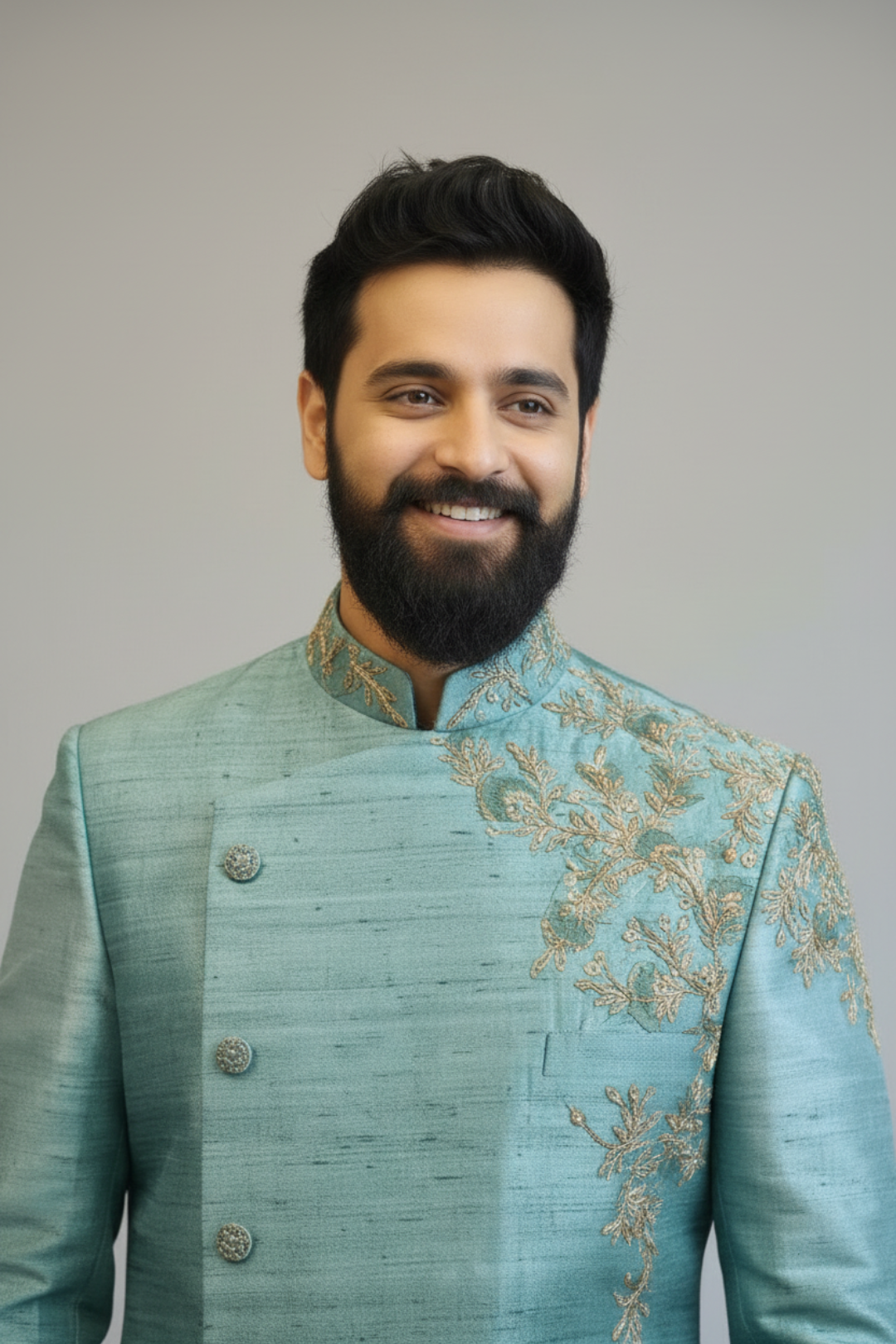 Man wearing a light blue embroidered traditional outfit against a plain background