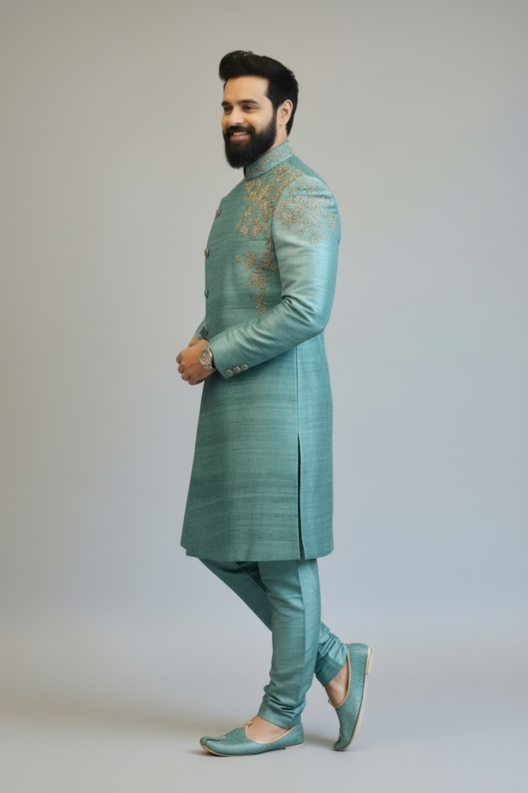 Man wearing a teal sherwani with intricate embroidery on a plain background