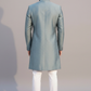 Man wearing a light blue sherwani with white pants on a gray background
