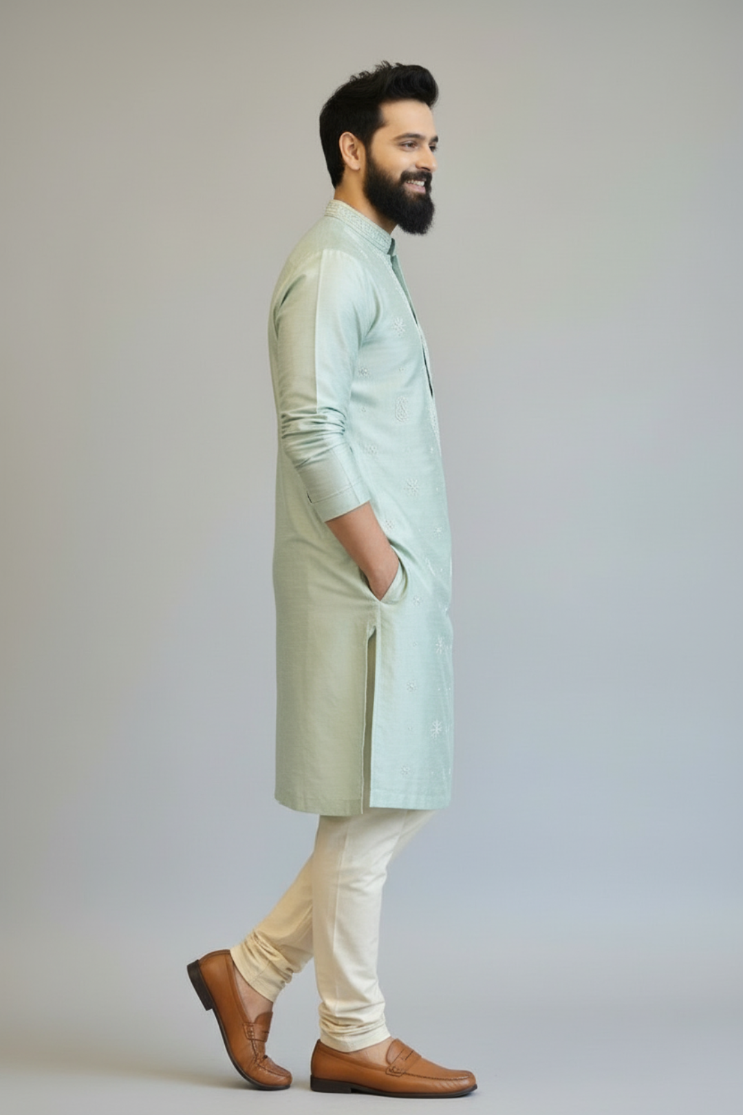 Man wearing a light green kurta with white pants and brown shoes on a plain background
