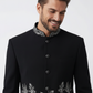 Man wearing a black coat with floral embroidery on a white background