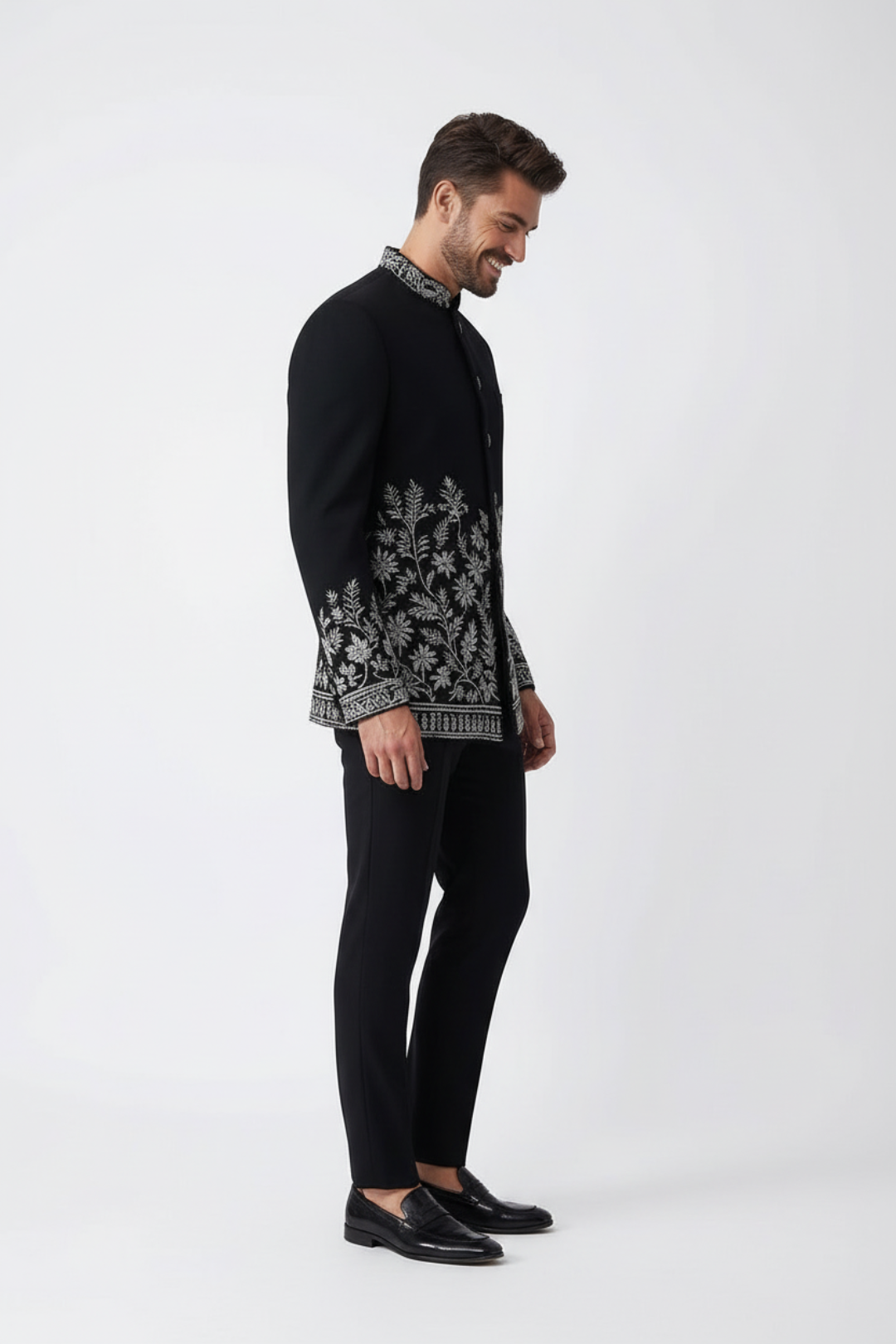 Man wearing a black embroidered jacket and black pants on a white background